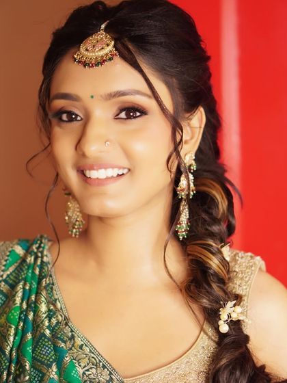 A full view of Nony's Mehendi look, complete with a beautiful side braid. The earthy makeup tones harmonize perfectly with her green and gold attire for a cohesive and elegant style.