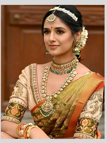 This cream-colored blouse features exquisite Kalamkari-inspired embroidery on the sleeves, paired with delicate zardosi work along the neckline. It is a perfect complement to the olive green Kanjeevaram saree.
