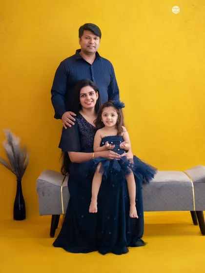 A lovely family portrait against a sunny yellow backdrop. Their coordinated blue outfits make the image pop with color and happiness.
