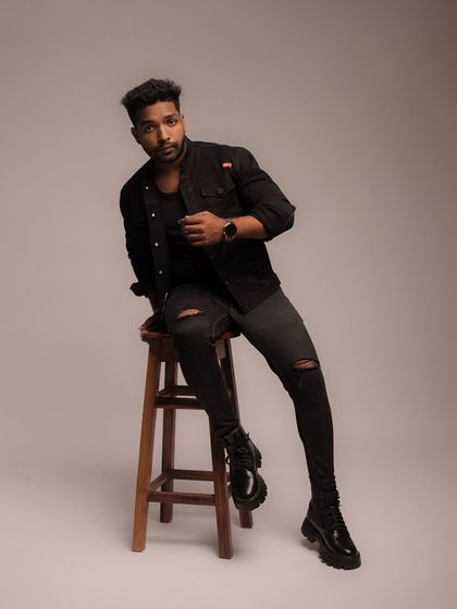 A seated portrait of a male model in an all-black outfit. The pose is confident and direct, perfect for a commercial or fashion look.