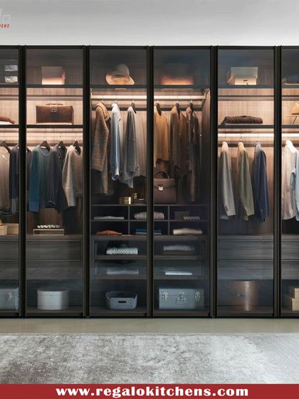 A full-wall wardrobe with smoked glass doors and dark wood interiors. The extensive shelving and hanging space provide a comprehensive storage solution for any collection.