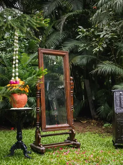 For a naming ceremony with a South Indian village theme, we used vintage furniture like this classic mirror and carved chest. These elements, set against a lush green lawn, helped bring the nostalgic 1990s theme to life.