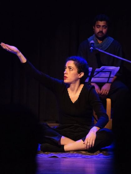 An actress performs a storytelling moment on stage, drawing the audience into the world of the folk tale. The minimalist staging puts the focus on the power of performance.