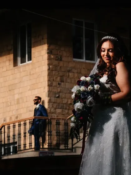 Using natural light and shadow to create a compelling composition. The bride is softly lit in the foreground while the groom stands in the background, creating a sense of story and anticipation.