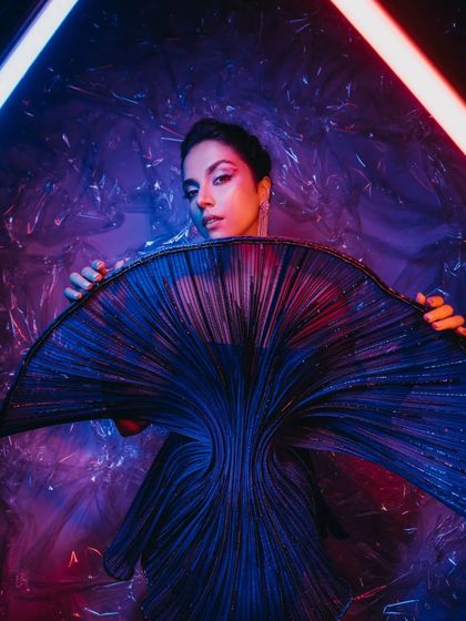 A model poses with a unique, fan-like prop against a backdrop of iridescent cellophane and neon lights. This is how we create a vibe for a super chilled-out after-party.