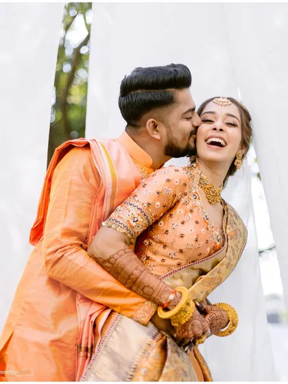 A sweet kiss on the cheek, a moment of pure joy and affection captured during a vibrant Haldi ceremony.