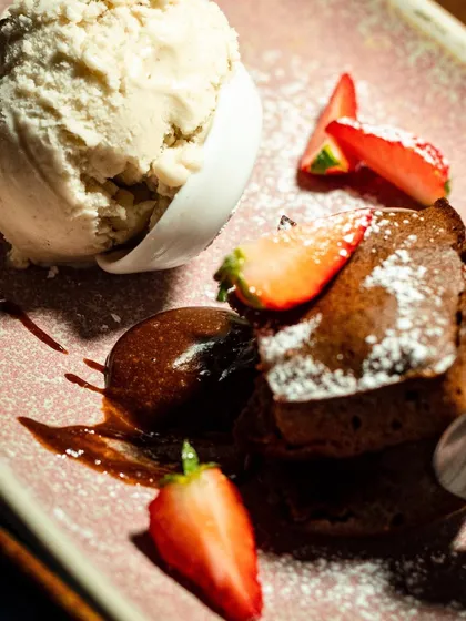 A gooey chocolate fondant with fresh strawberries and ice cream. The composition is dynamic, with the elements arranged to lead the eye around the plate.