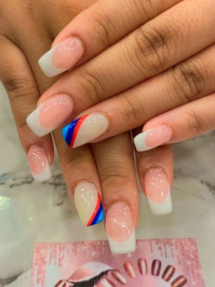 A classic French manicure with a subtle, patriotic twist. The ring finger is accented with thin, diagonal stripes of red and blue.