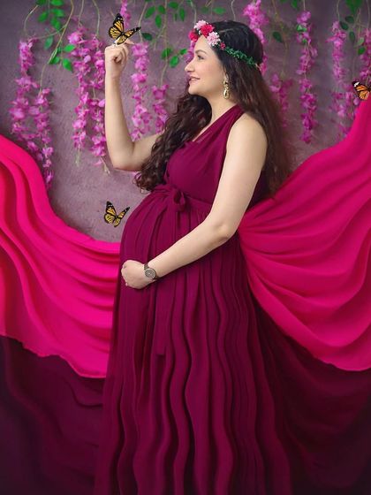 Feeling like a goddess in this whimsical studio setup. The flowing magenta gown, flower crown, and magical butterflies create a truly enchanting maternity portrait.