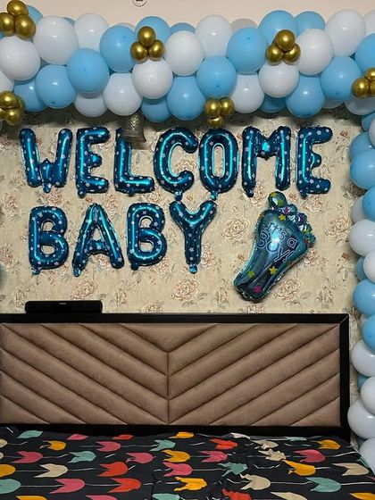 Another style for a bedroom welcome decoration. This setup features a full balloon frame around the headboard in blue, white, and gold, with "WELCOME BABY" foil balloons in the center.