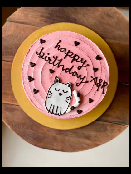 A cute pink birthday cake with a hand-drawn cat illustration.