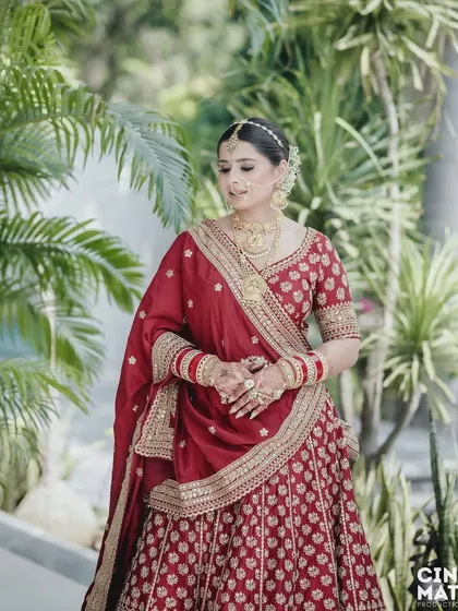 A full-length shot of the bride in her stunning red lehenga, set against a lush green background that makes her colors pop.