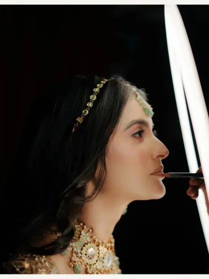 A behind-the-scenes shot of the bride getting her makeup done, the lighting creating a dramatic and artistic effect.