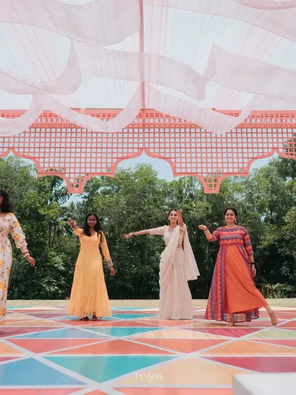 A colorful dance performance at a daytime Mehendi event. The stage features a vibrant, multi-colored floor and a pink canopy, creating a joyful and high-energy setting.