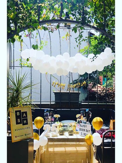 A wider view of the sunny 25th birthday setup. The white balloon garland hanging from the ceiling creates a dreamy, cloud-like effect over the beautifully decorated party table.
