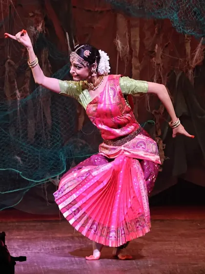 Performing a solo piece within the "UNMASKED" production. The stage design, featuring fishing nets, and the vibrant pink costume help create the world of ancient Lanka.