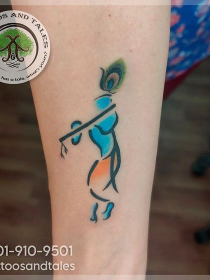 A minimalist Lord Krishna tattoo using simple lines and a splash of color. The design captures the essence of Krishna with his flute and a peacock feather, perfect for a subtle yet meaningful piece.