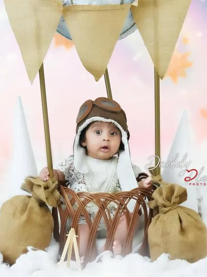 A closer shot of the baby in the hot air balloon setup, showing the details of the basket and the baby's cute pilot hat.
