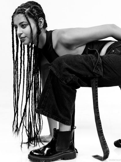 A low-angle shot from the braids series, emphasizing the model's boots and strong pose.