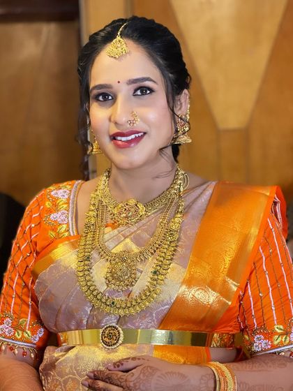A close-up of Yashaswini on her baby shower day. Her makeup is bright and celebratory, matching her orange silk saree.