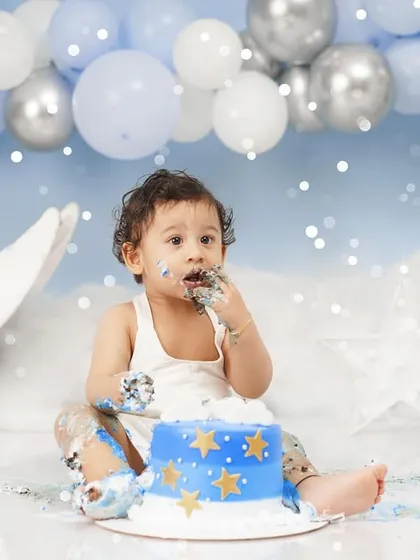 A baby boy gets his first taste of cake during a 'Moon & Stars' themed cake smash, with blue and silver balloons creating a festive atmosphere.