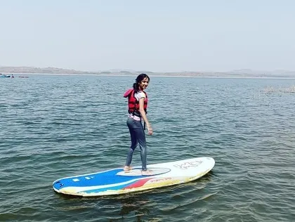 A girl smiles as she successfully balances on her paddleboard at Vani Vilas Sagar.