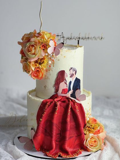 A personalized two-tiered anniversary cake featuring a custom couple illustration. The bride's red dress is made from flowing, edible fabric, adding a unique 3D element.