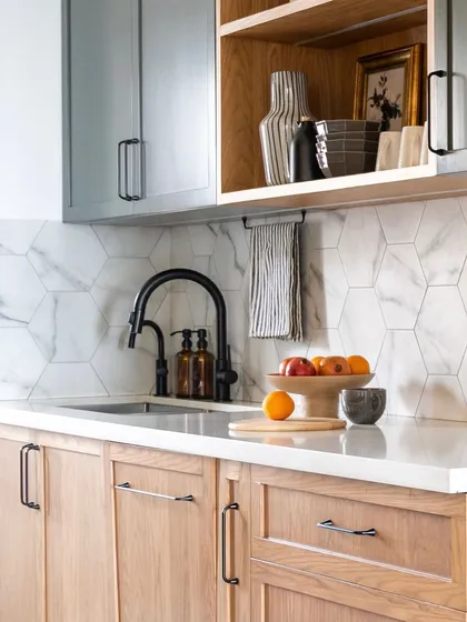 This kitchen beautifully balances warm wood tones with cool grey. The hexagonal marble backsplash adds a layer of subtle pattern, while the open shelving provides a space to display personal items, making the kitchen feel lived-in and curated.