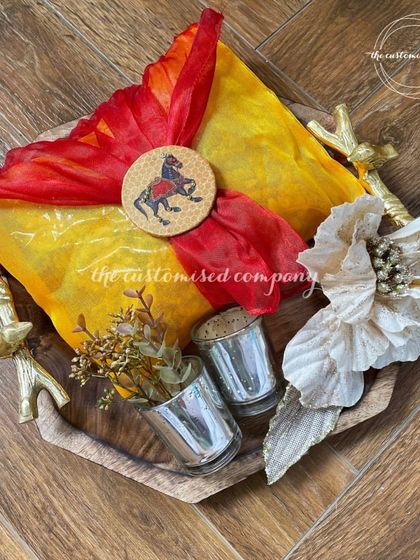 I designed this unique Diwali hamper on a beautiful wooden tray with ornate metal handles. It features shot glasses for serving and a colorful bandhani-wrapped gift, blending rustic charm with festive tradition.