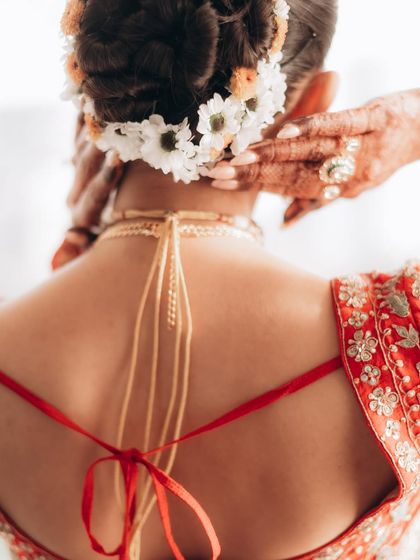 A detail-oriented shot of the bride's hair adorned with fresh flowers and the tie of her blouse. This focuses on the traditional elements and artistry of the bridal look.