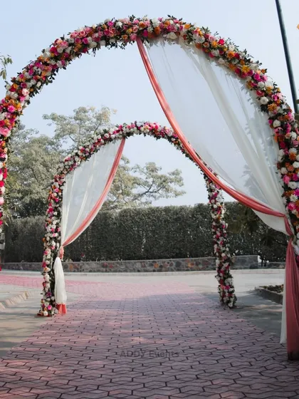 A grand entrance composed of two massive floral arches, draped with soft, flowing fabric. This creates a spectacular and romantic gateway for any wedding celebration.