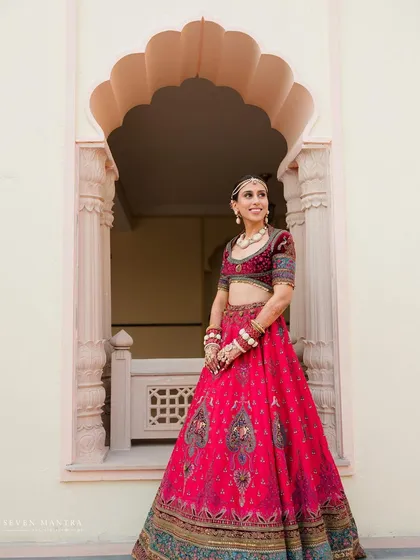 A portrait of pure joy. I styled Anokhi in a vibrant jewel-toned lehenga, using the classic arches of the palace as a natural frame to highlight her radiant smile and majestic bridal look.