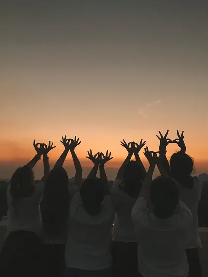 Students form mudras with their hands against the sunset. This beautiful, silhouetted image captures a moment of collective peace and reverence for the end of the day.