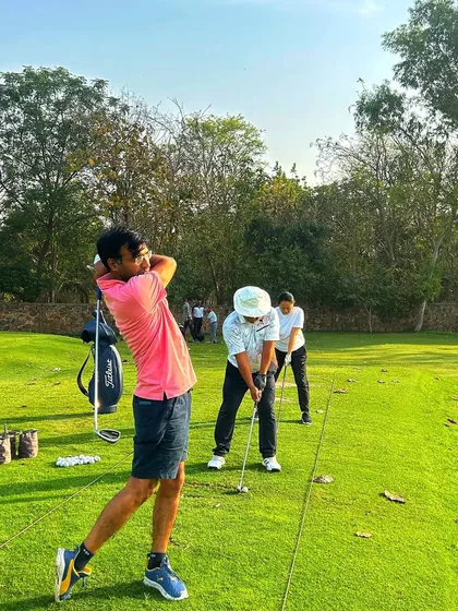 A golfer in a bright pink shirt completes his swing, adding a splash of color to the greens.