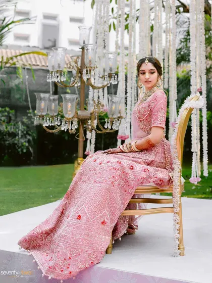 A poised and elegant portrait of the bride seated on a golden chair, her pink lehenga spread beautifully around her.
