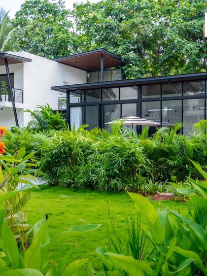 This villa showcases a clean, modern aesthetic with its white facade, dark metal accents, and extensive use of glass. The design is both elegant and perfectly integrated with its natural surroundings.