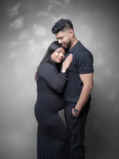 A classic portrait of togetherness. Dressed in elegant black, their pose is one of quiet strength and unity. The painterly backdrop adds a timeless quality to this beautiful maternity photograph.