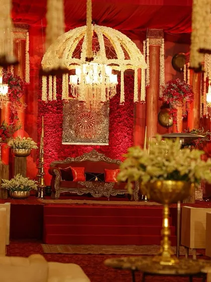 The couple's seating area, framed by cascading floral chandeliers and set against a backdrop of deep red, creating a focal point of regal elegance.