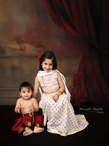 A beautiful portrait of a big sister and her baby brother, both dressed in traditional Indian attire. Her gentle guidance and his curious look create a truly special moment.