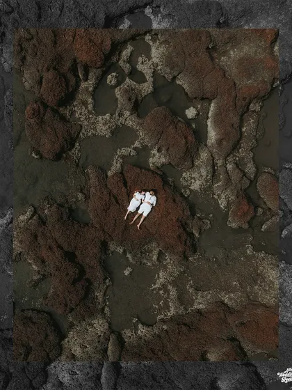 A breathtaking top-down drone photograph of a couple in white, finding a moment of peace on the rustic, rocky shores of Goa.