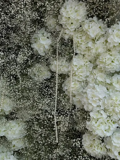 A texture-rich close-up of the floral backdrop, showing the interplay between fluffy baby's breath, white hydrangeas, and delicate pearl strings.