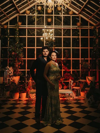 An atmospheric maternity portrait of a couple in a beautifully lit, greenhouse-style room at night. Her shimmering gown and his dark attire create a moody, romantic feel, showing a different, more intimate side of maternity photography.