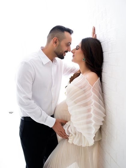 An intimate high-key portrait. The couple's close pose against the white brick wall creates a modern and romantic feel.