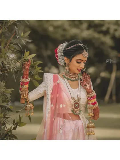 A full-length portrait of a bride in her stunning white and pink lehenga, showing off her traditional kalire. The natural, outdoor setting adds a soft touch.