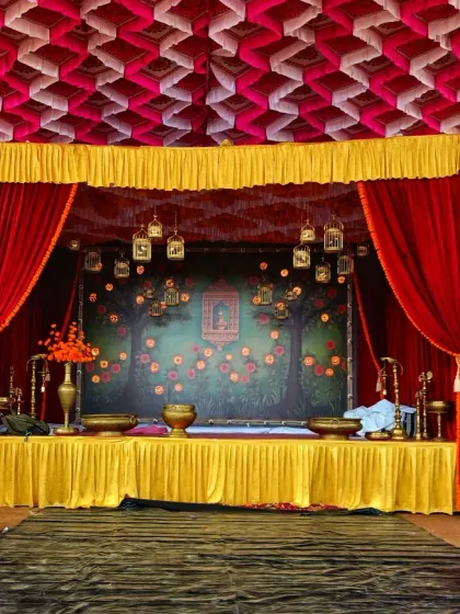 A unique stage design with a theatrical feel, using red and yellow curtains, a decorative ceiling, and a painted backdrop for a themed sangeet night.