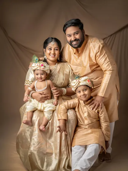 A beautiful family dressed in traditional golden attire, celebrating their little Krishna.