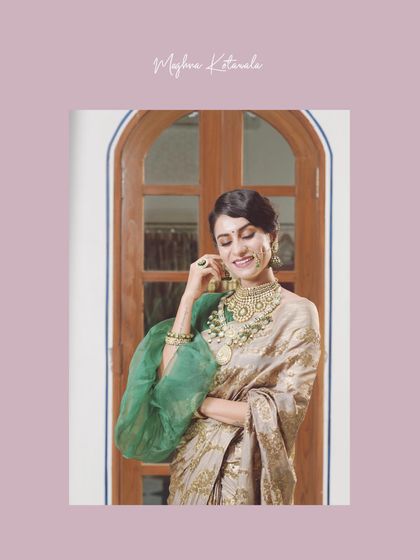 The bride looking elegant against a classic arched doorway. The puff sleeves of her green blouse add a modern touch to the traditional saree, a signature element of our styling approach.