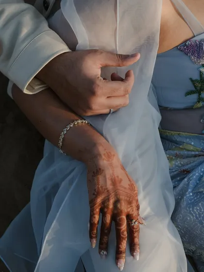 A close-up on intertwined hands, showcasing the bride's henna and engagement ring. We believe in capturing the small details that tell a larger story of commitment and culture.