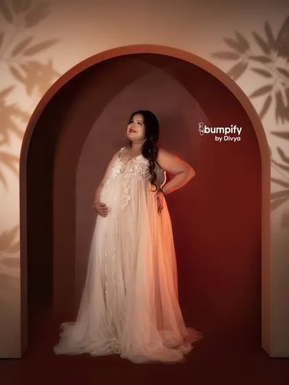A stunning solo portrait in our new red arch setup. The play of light and shadow creates a dramatic and artistic effect, highlighting the mom-to-be in her beautiful white gown.