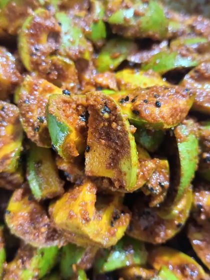 A close-up of the mango pickle preparation. The combination of green mango skin and yellow flesh with dark spices looks as good as it tastes.